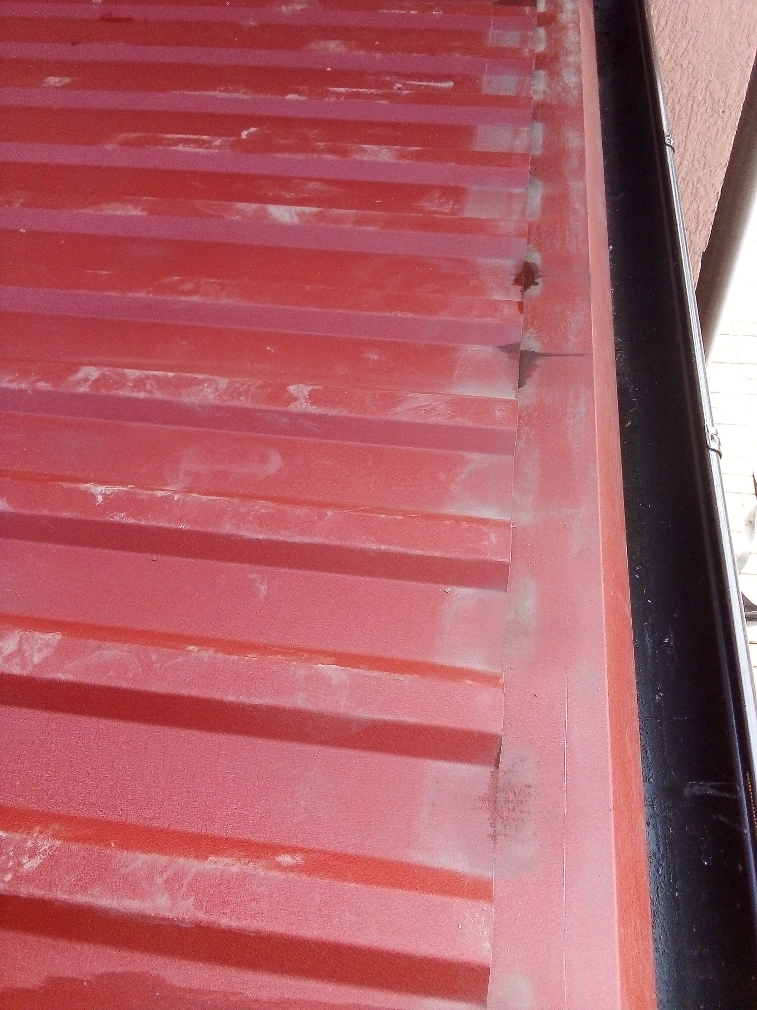 Czerwona, pomalowana blacha trapezowa na elewacji budynku, widoczne ślady zabrudzeń i zacieków, obok rynna spustowa.