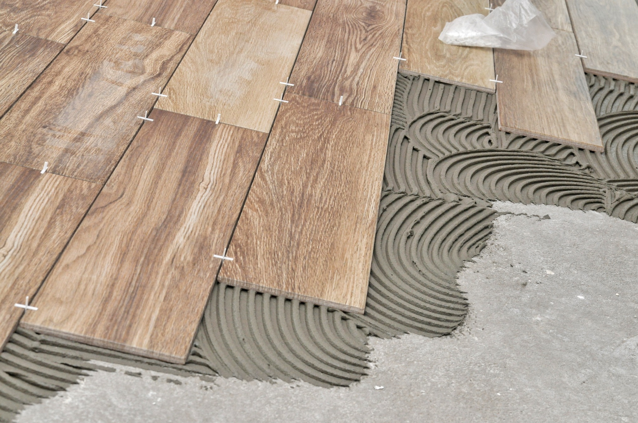 Proces układania podłogi z płytek imitujących drewno, widoczne krzyżyki dystansowe i warstwa kleju z charakterystycznymi rowkami.