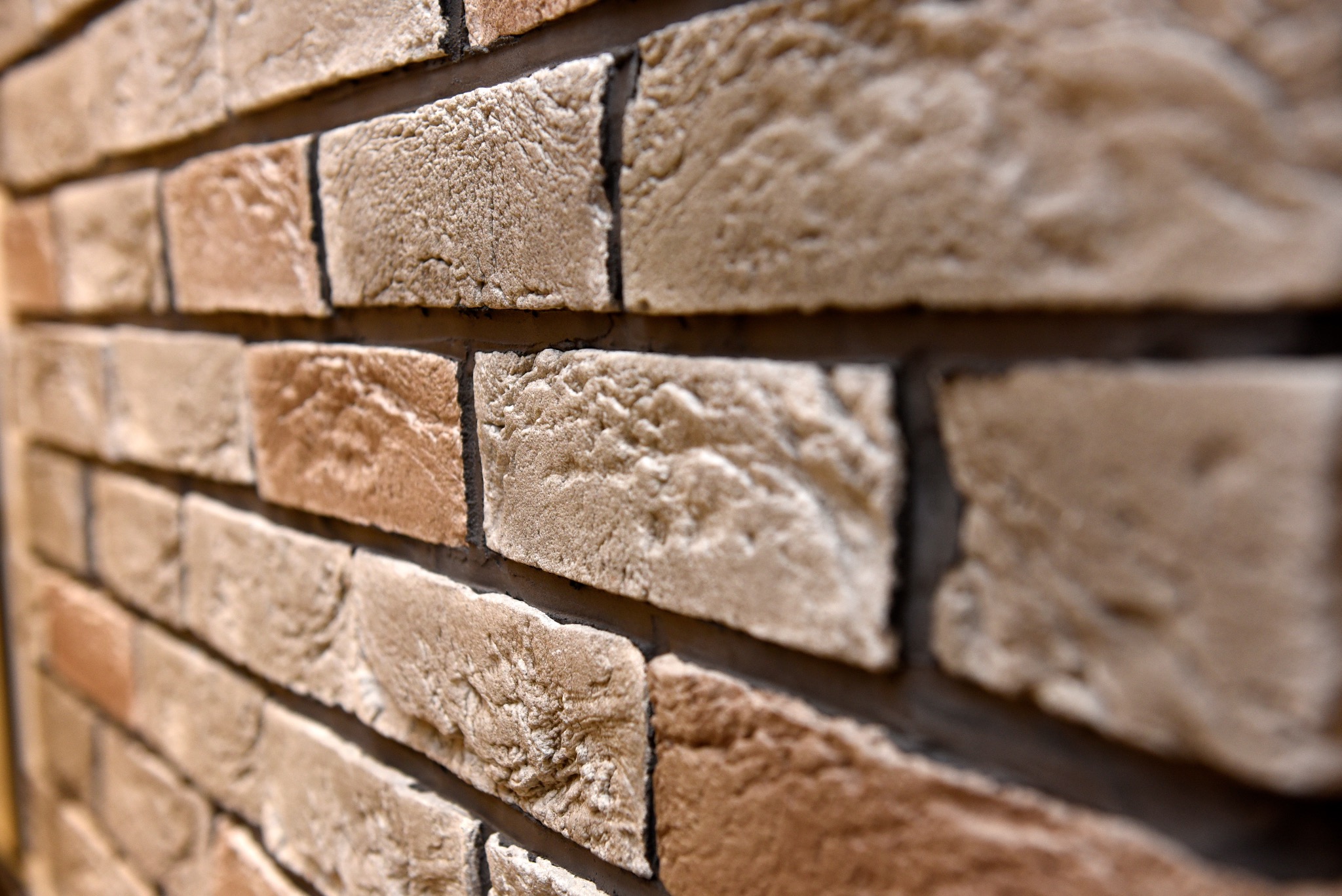 Ściana wykończona dekoracyjną cegłą w odcieniach beżu i brązu, z wyraźną fakturą i ciemnymi fugami, ujęcie pod kątem z bliska.