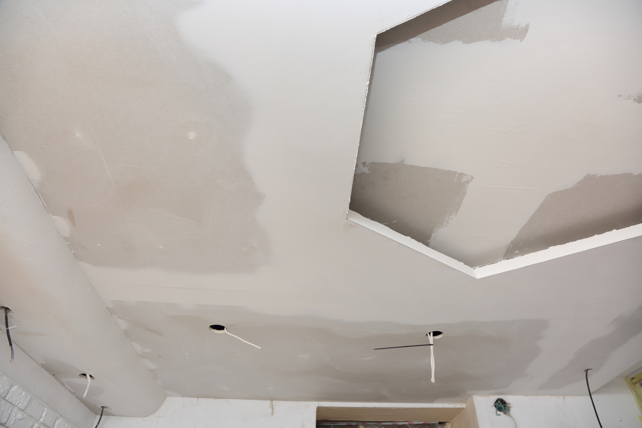 Niedokończony sufit z płyty kartonowo-gipsowej, widoczne otwory na oświetlenie i fragmenty niezaszpachlowane, zarys wnęki w suficie.