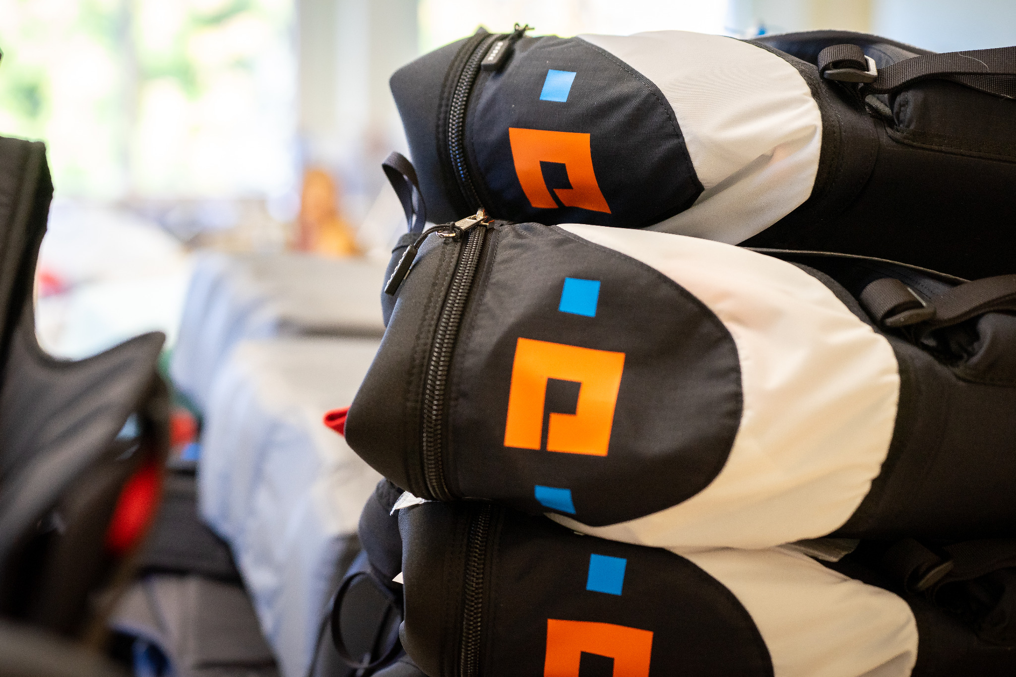 Stos czarno-białych pokrowców z pomarańczowo-niebieskim logo, widoczne zamki błyskawiczne i paski mocujące.