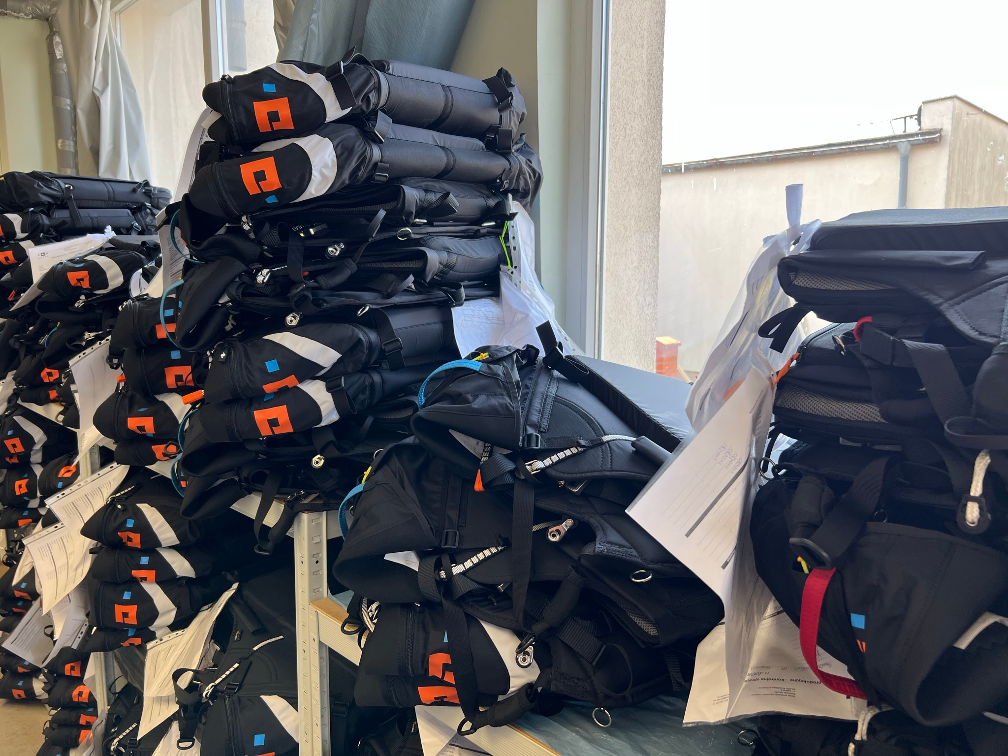 Stosy uszytych, czarnych pokrowców z kolorowymi elementami, ułożonych na półkach w szwalni, widoczne faktury i detale materiału.