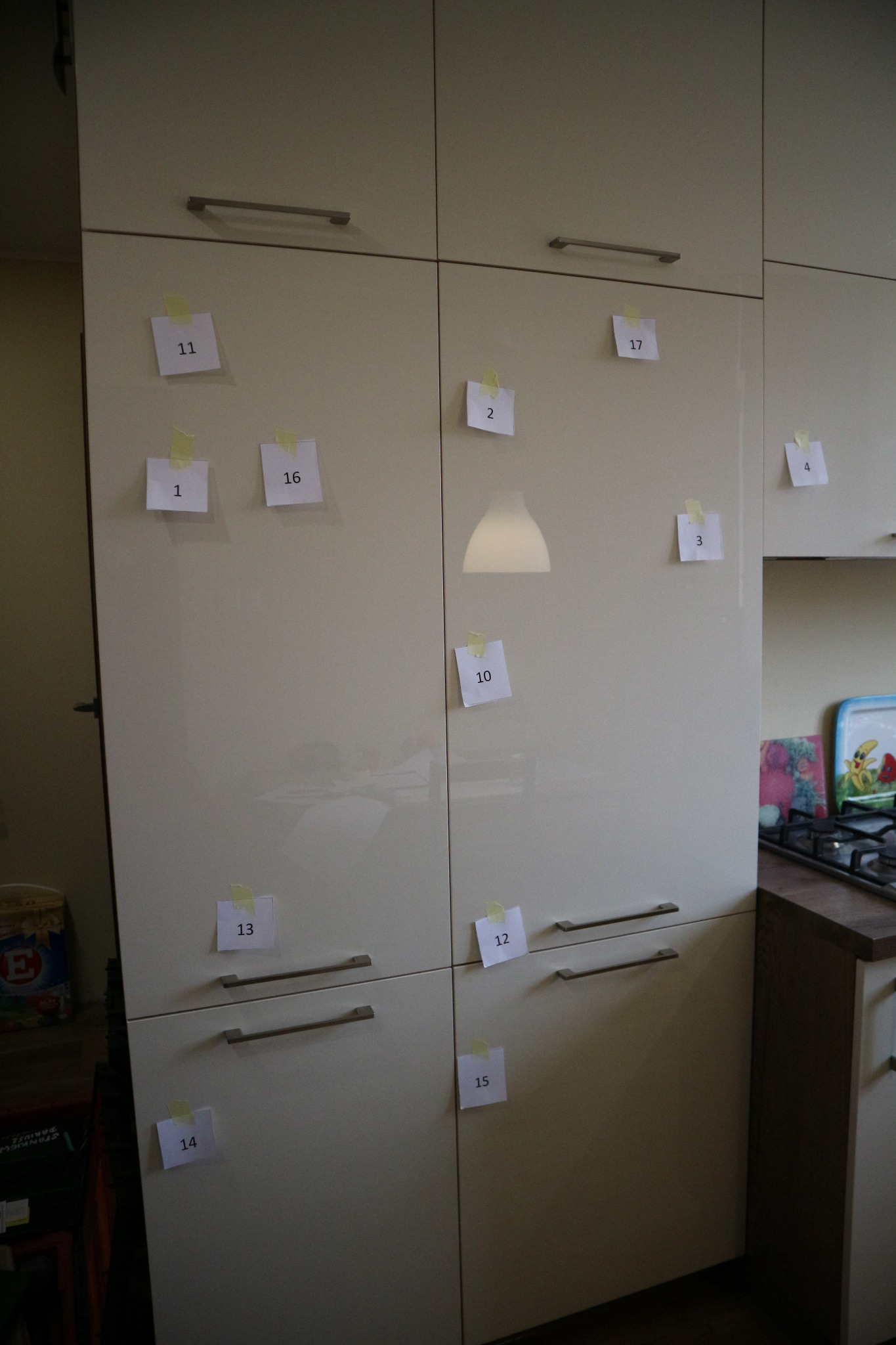 Ocena jakości montażu mebli kuchennych: szafki oznaczone ponumerowanymi karteczkami samoprzylepnymi, prawdopodobnie wskazującymi na wady lub niedociągnięcia.