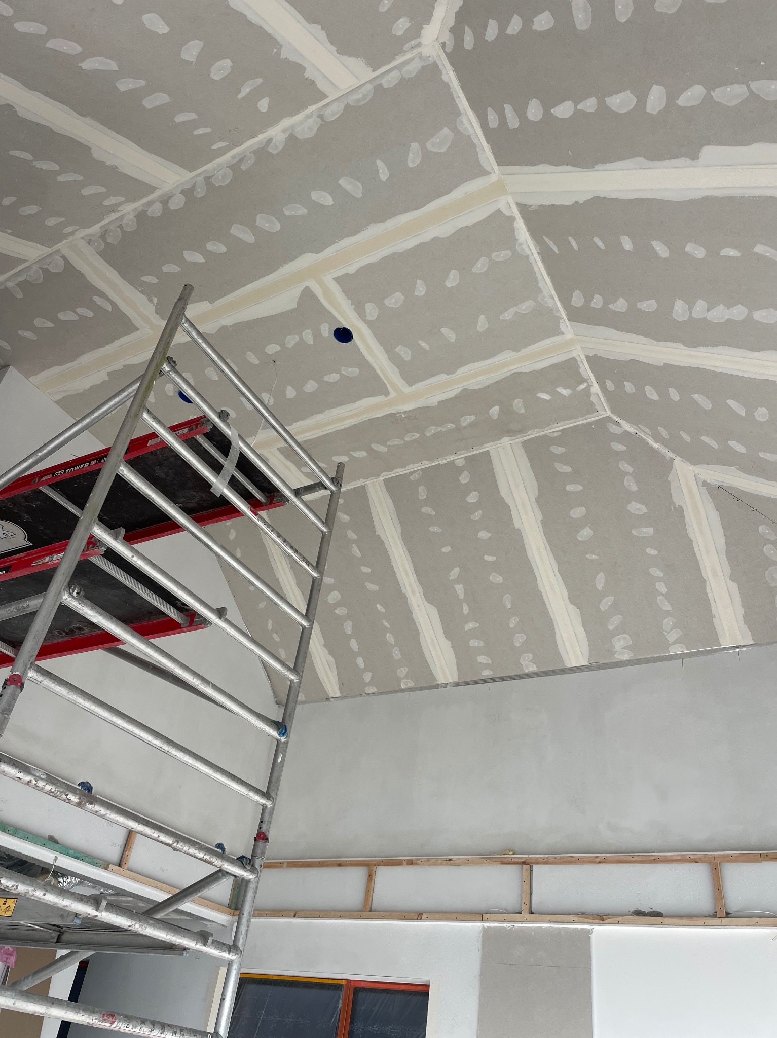 Skośny sufit z płyt kartonowo-gipsowych, częściowo zaszpachlowany, widoczny z poziomu rusztowania. Otwory na oświetlenie punktowe.