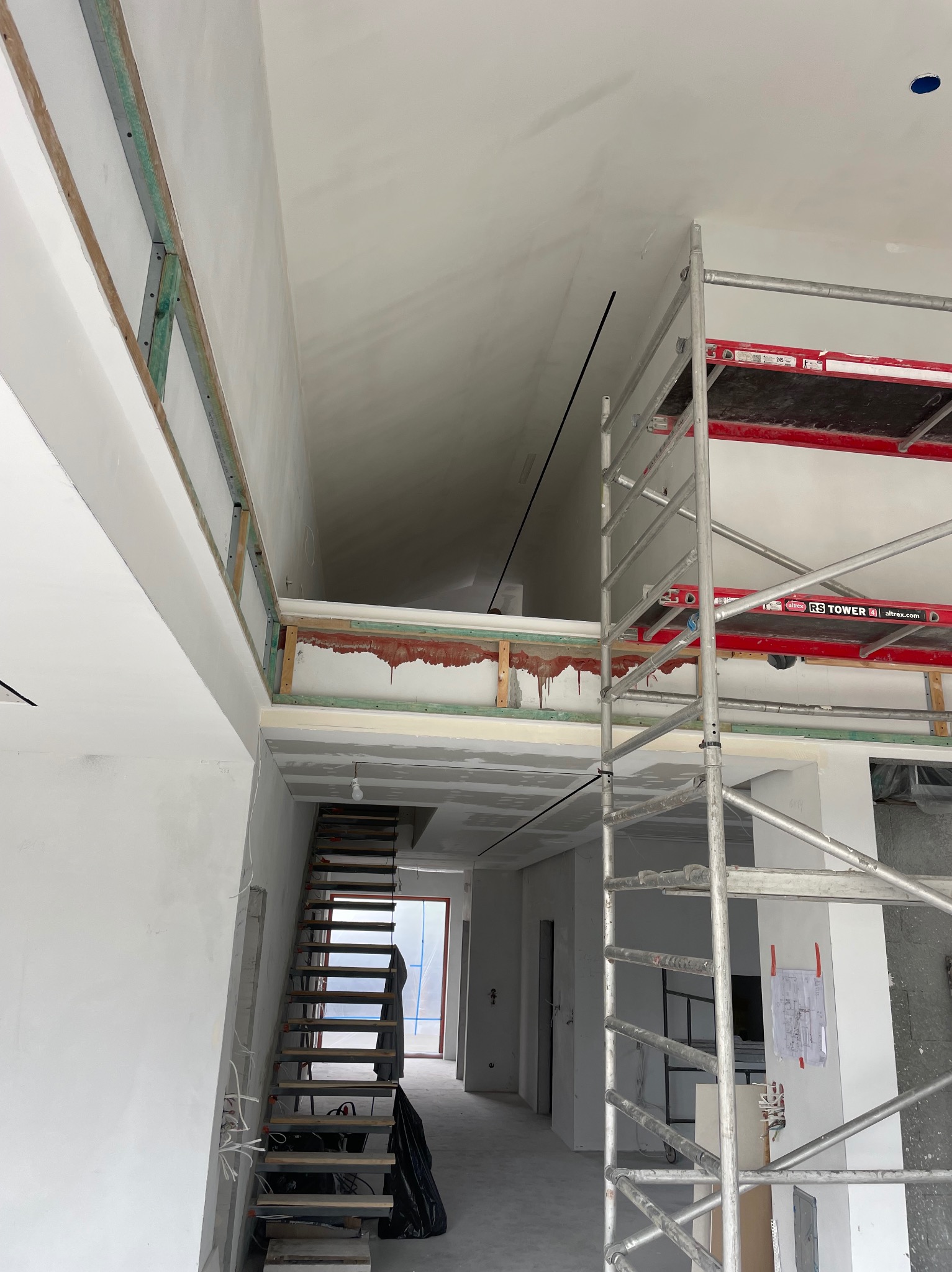 Wnętrze w trakcie prac wykończeniowych: widoczne rusztowanie, schody, ściany przygotowane do malowania, elementy konstrukcyjne poddasza. Surowy stan, jasne kolory.