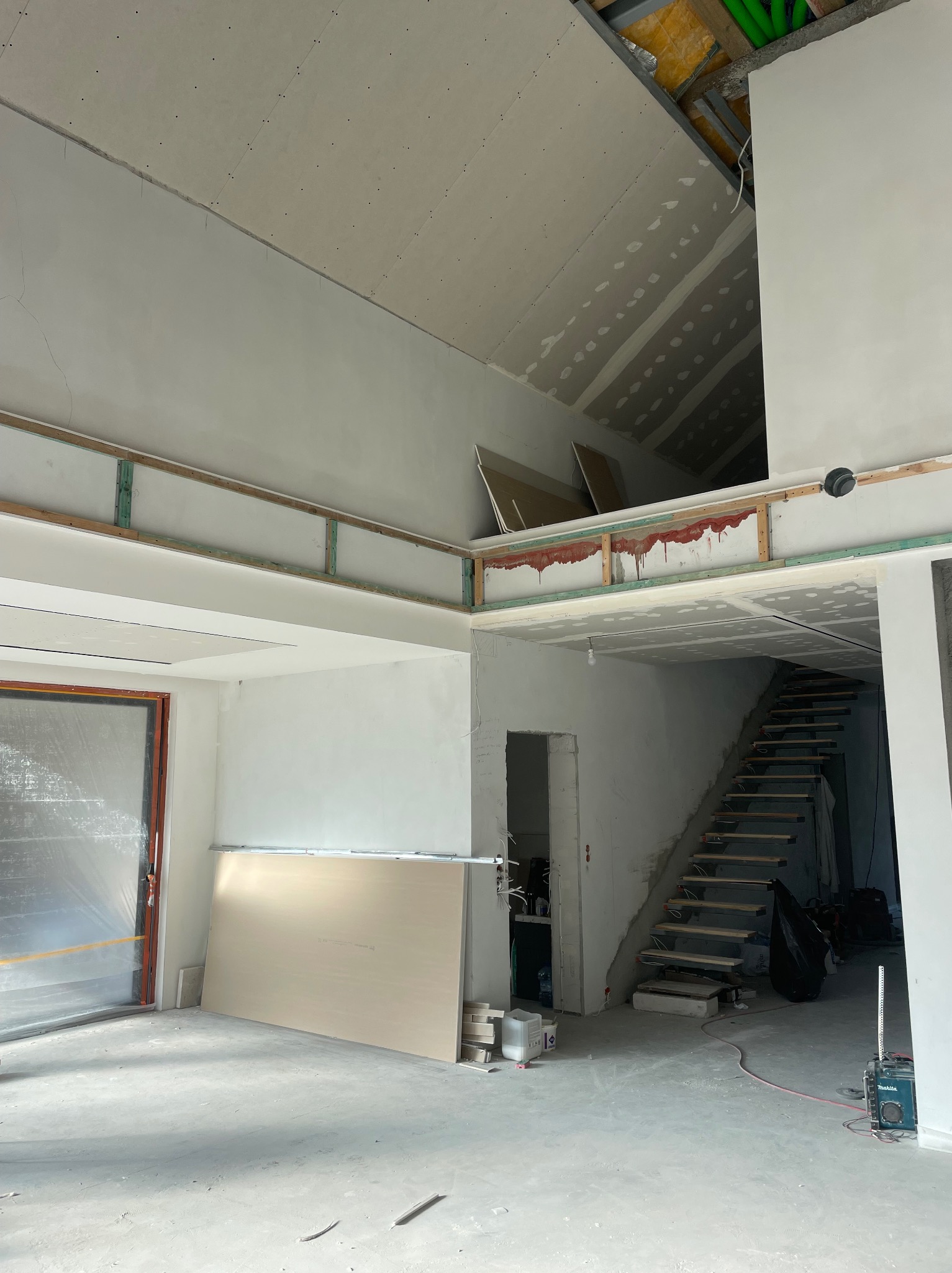 Wnętrze w trakcie prac wykończeniowych: płyty karton-gips na suficie, widoczne schody i przygotowane ściany. Elementy instalacji pod sufitem.