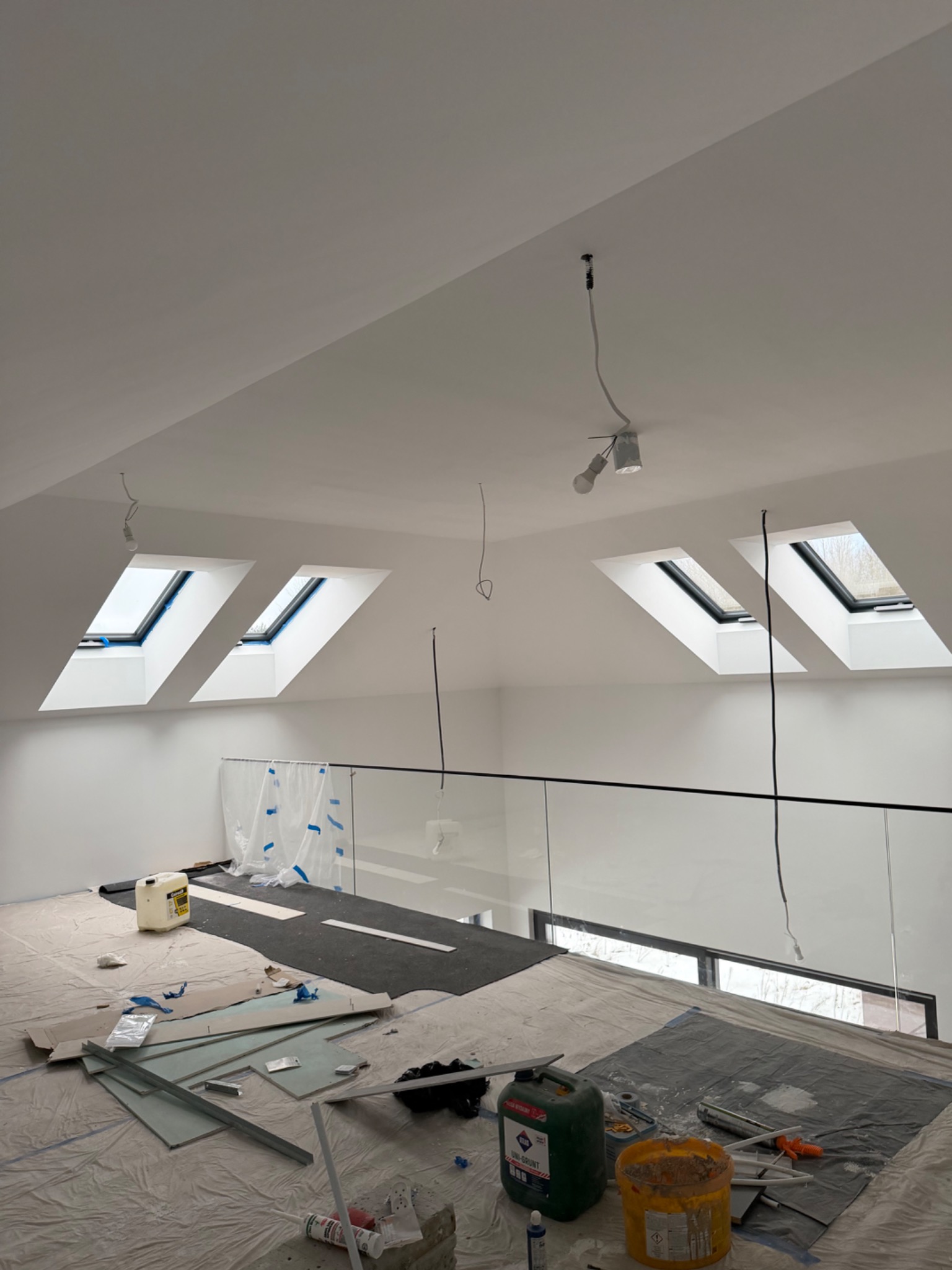Poddasze w trakcie prac wykończeniowych: widoczne okna dachowe, materiały budowlane, zabezpieczona podłoga. Ściany pomalowane na biało.