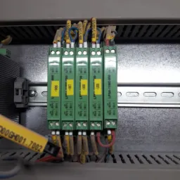 Szyna DIN z zamontowanymi, oznaczonymi modułami zabezpieczającymi LPSA-11ME-000, podłączonymi kablami z żółtymi oznaczeniami, w szarej szafie sterowniczej.