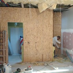 Kipish-Master Mykola Choban - Wnętrze w trakcie prac remontowych: ściany obłożone płytami OSB, izolacja stropu wełną mineralną, pracownik szpachluje ścianę, widoczne narzędzia i materiały budowlane.