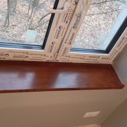 Kipish-Master Mykola Choban - Zamontowany brązowy parapet pod oknem dachowym marki Gealan, widok z wnętrza pomieszczenia na jesienne drzewa.