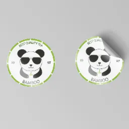 Dwa okrągłe, białe naklejki z logo pandy w okularach, trzymającej filiżankę z bambusem, otoczone zielonym obramowaniem z napisem 'Best Quality Tea' i 'Bamboo', jedna z naklejek jest częściowo...
