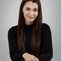 MARTA KOTECKA - Portret uśmiechniętej brunetki w czarnym golfie, opierającej dłonie na szarym krześle, z widocznym logo fotografa w lewym górnym rogu.