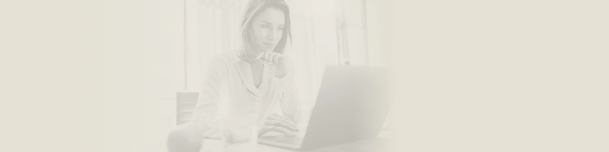 Kobieta w białej koszuli skupiona na pracy przy laptopie. Dłoń podparta pod brodą, w tle okno i regał. Stonowana kolorystyka.