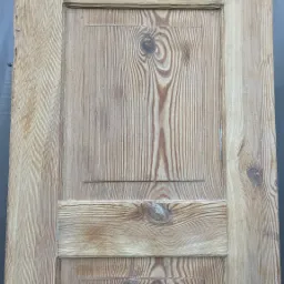 Stara, drewniana płycina drzwiowa z widocznymi śladami użytkowania i zamkiem, ukazująca naturalny rysunek słojów drewna.