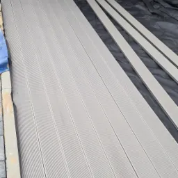 Montaż szarego tarasu kompozytowego w Stargardzie, widoczne deski, podłoże z czarnej folii i fragment osoby w jeansach.