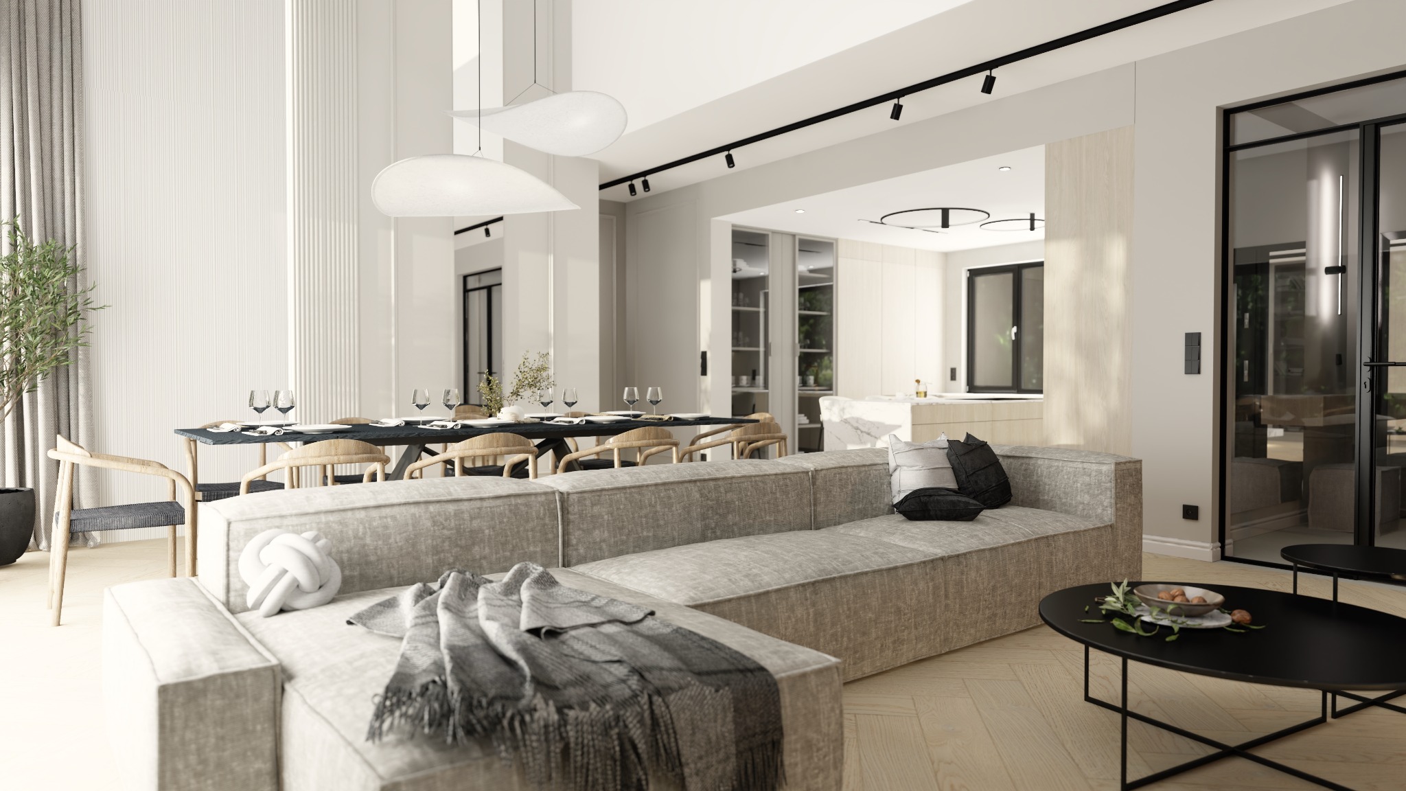 Jasne, przestronne wnętrze: salon przechodzi w jadalnię z długim stołem nakrytym do posiłku, a w tle widoczna kuchnia z marmurowym blatem. Na pierwszym planie szary narożnik z dekoracyjnym węzłem...