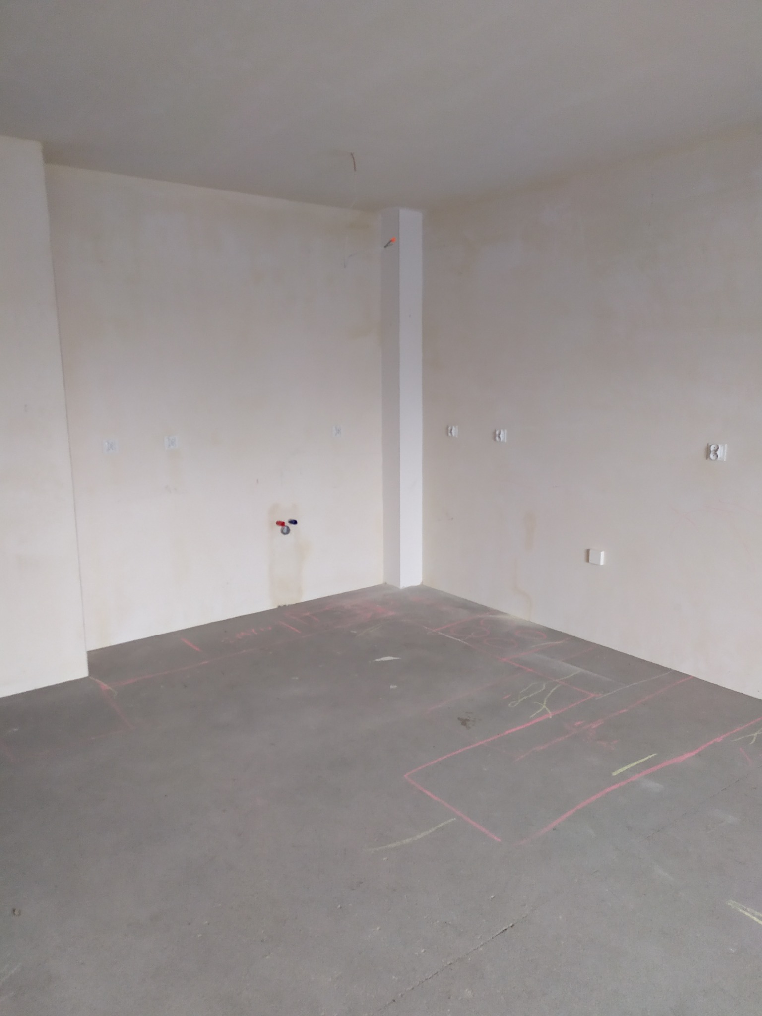 Surowe wnętrze łazienki w trakcie remontu, z widocznymi instalacjami i planem rozkładu płytek narysowanym na podłodze.