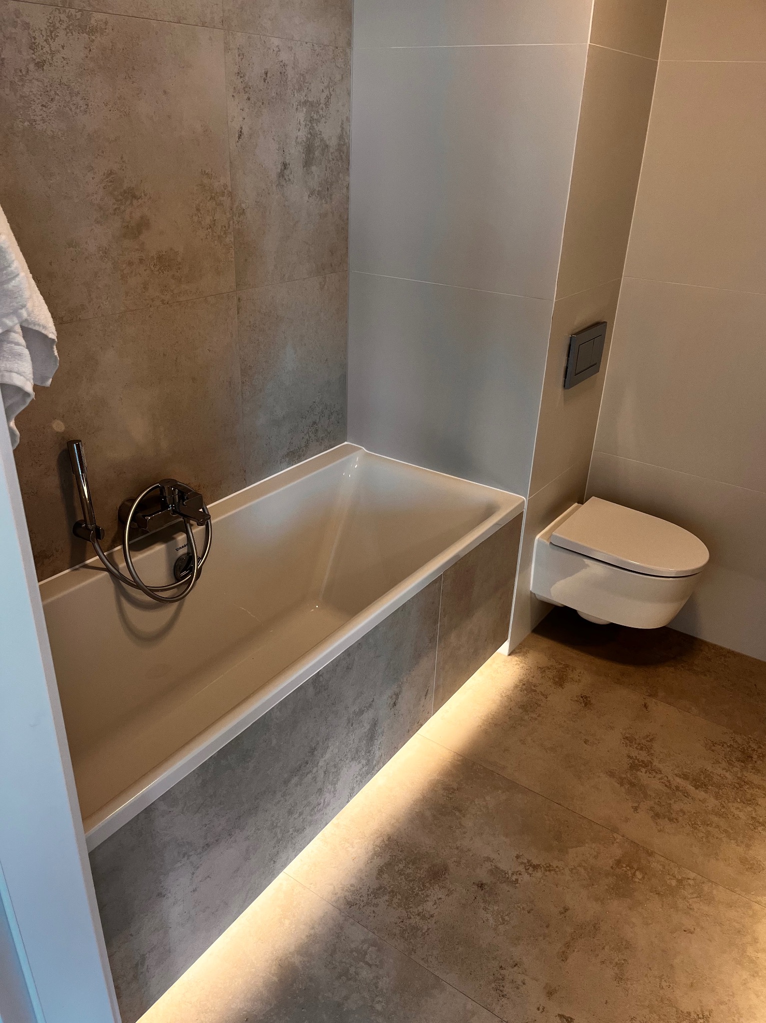 Nowoczesna aranżacja łazienki w Poznaniu z podświetloną wanną, wiszącą toaletą i płytkami imitującymi kamień na ścianach i podłodze.