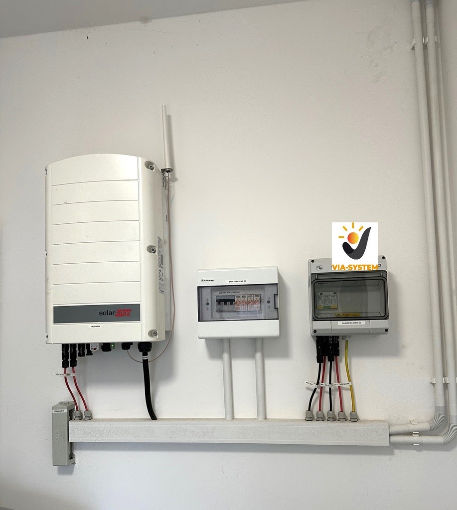 Instalacja elektryczna wewnątrz budynku z widocznym inwerterem SolarEdge, skrzynkami zabezpieczeń i okablowaniem poprowadzonym w listwach przypodłogowych.