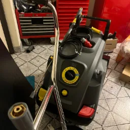 Wysokociśnieniowa myjka Karcher z akcesoriami, w tle czerwone szafki warsztatowe i wzorzysta podłoga.