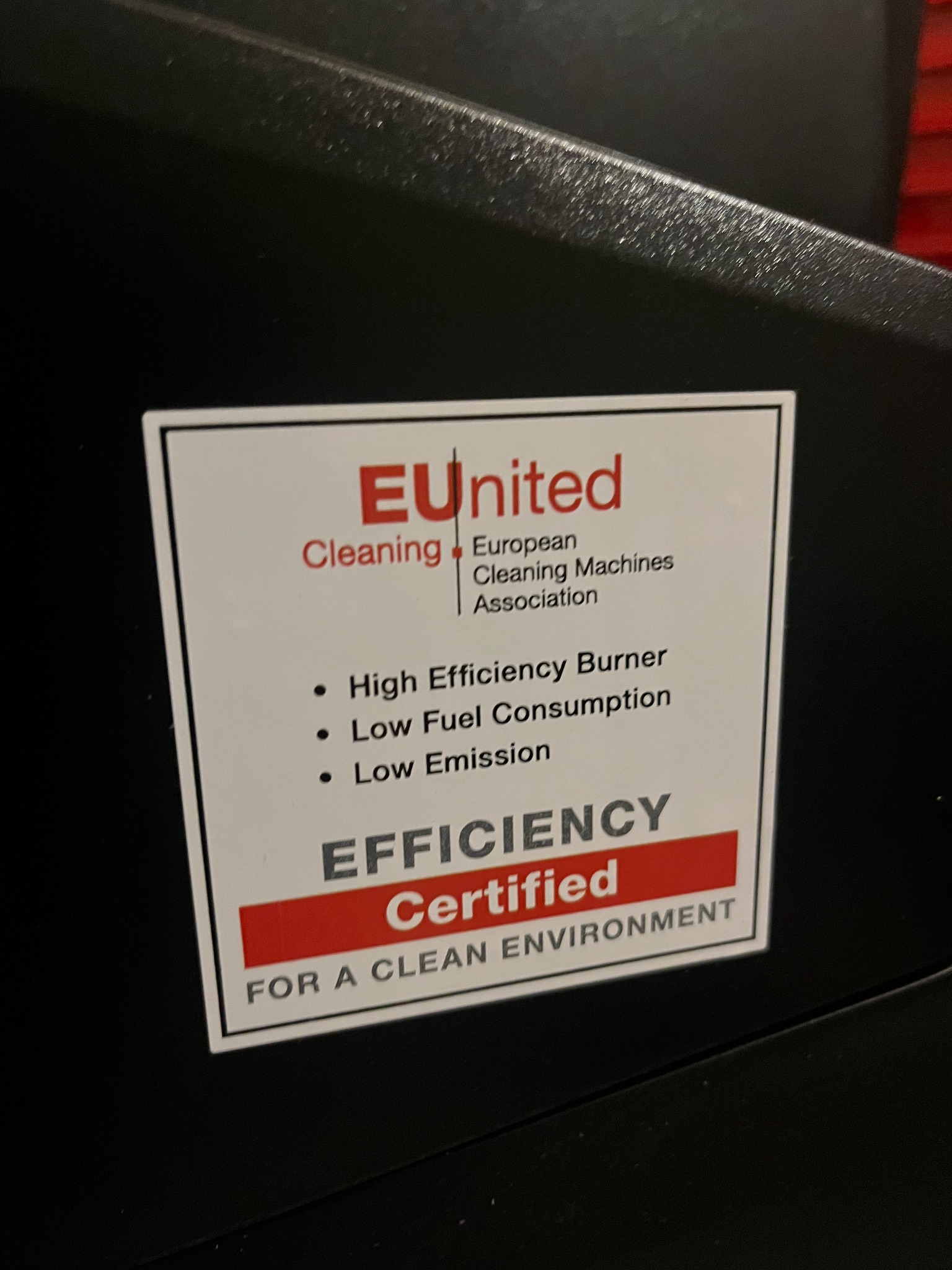 Etykieta z logo EUnited Cleaning, informująca o certyfikowanej efektywności i niskiej emisji, umieszczona na czarnej obudowie maszyny czyszczącej.