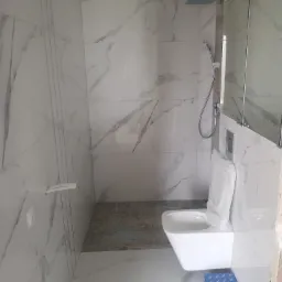 Nowoczesna łazienka z białymi płytkami imitującymi marmur, wisząca toaleta z otwartą deską i pudełko z akcesoriami na podłodze.