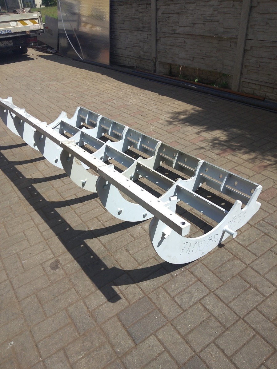 Malowana na szaro, stalowa konstrukcja kratowa z elementami półokrągłymi, leżąca na brukowanej nawierzchni, z widocznym napisem '710030 2551'.