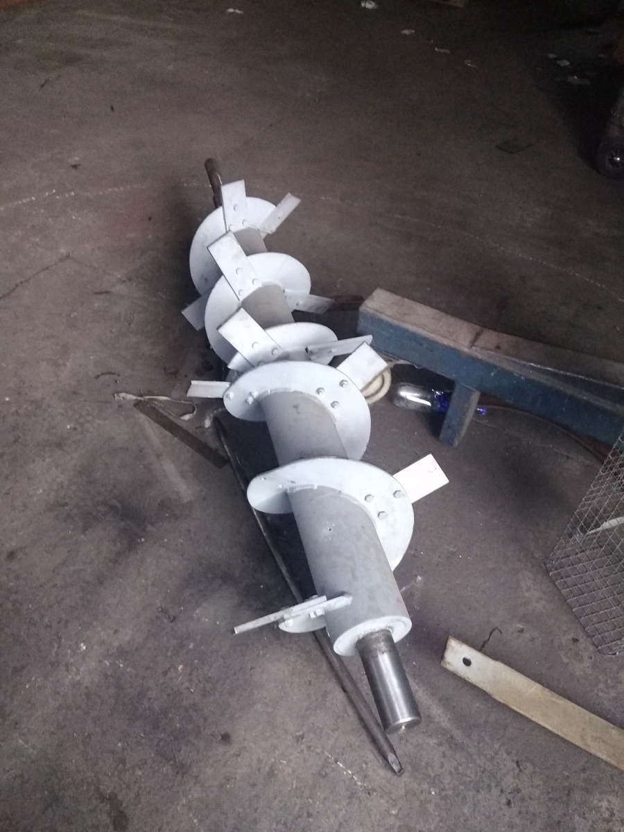 Metalowa spirala ślimakowa z przyspawanymi elementami, leżąca na betonowej posadzce warsztatu, widoczne ślady obróbki i montażu