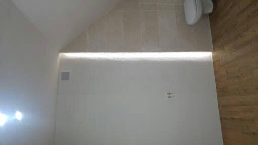 Wykończona łazienka na poddaszu ze skośnym sufitem, jasne płytki na ścianie, podświetlenie LED, drewnopodobna podłoga i toaleta podwieszana.