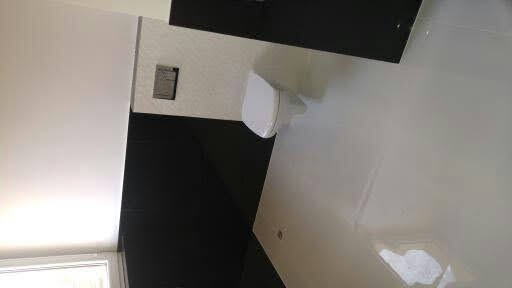 Biała, błyszcząca posadzka w łazience z czarnymi płytkami na ścianie, widoczne fragmenty toalety i czarnej szafki umywalkowej.