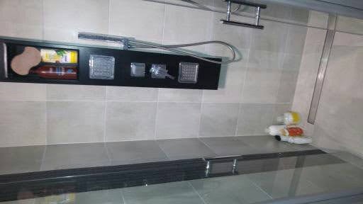 Wykończona łazienka z szarymi płytkami, czarną półką z akcesoriami prysznicowymi i szklanym panelem prysznicowym