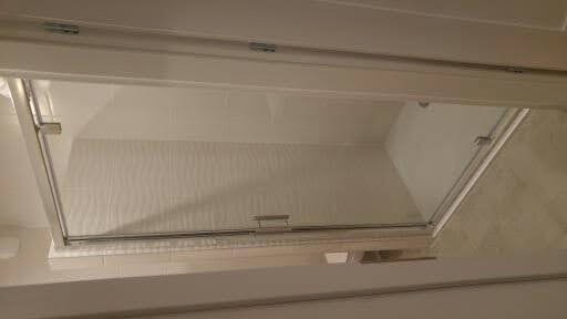 Szklana kabina prysznicowa z przesuwnymi drzwiami, widok z dołu, białe płytki na ścianach z delikatnym wzorem falistym.