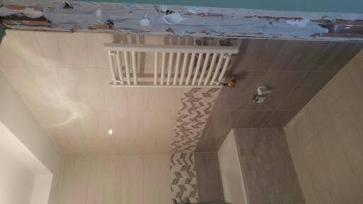 Wykończona łazienka z płytkami w odcieniach beżu i szarości, grzejnik drabinkowy na ścianie, dekoracyjny pas płytek w zygzaki.