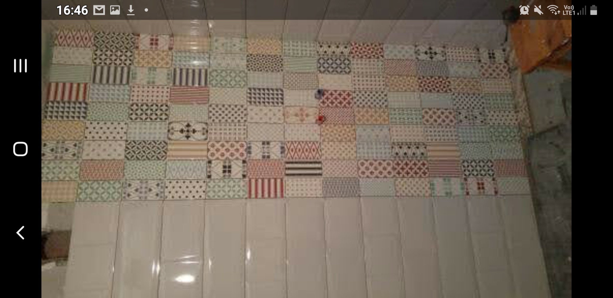 Ściana w łazience wyłożona różnokolorowymi, wzorzystymi płytkami ceramicznymi w stylu patchwork, z dolną częścią wykończoną dużymi, podłużnymi, białymi płytkami.