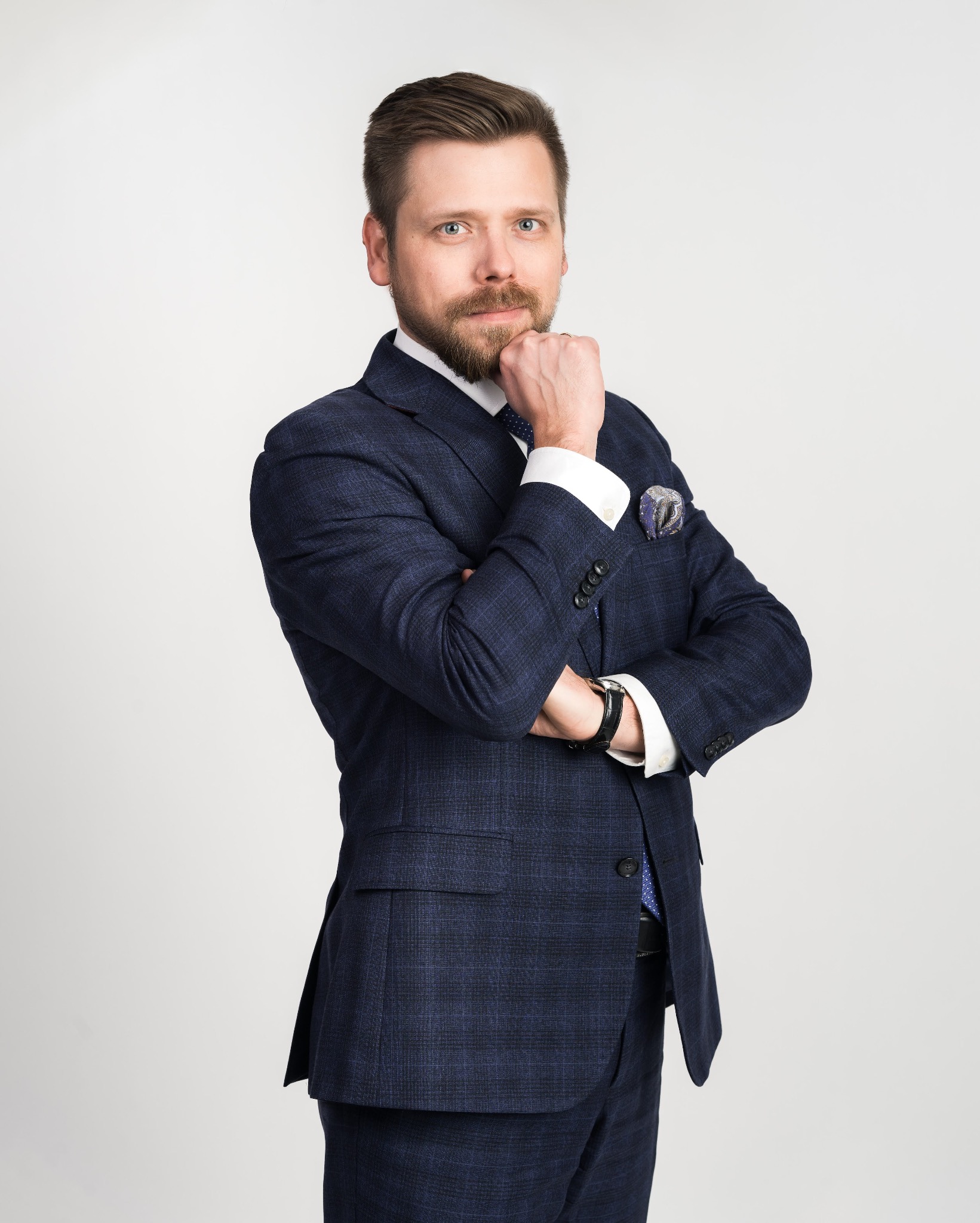 Portret mężczyzny w granatowym garniturze w kratę, z ręką podpierającą brodę, na jasnym tle.