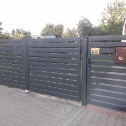 Nowoczesna, pozioma brama wjazdowa w kolorze grafitowym z brązową skrzynką na listy i tabliczką ostrzegawczą 'Uwaga! Zły pies', widoczna z zewnątrz posesji.