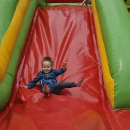 Uśmiechnięty chłopiec zjeżdża na czerwonym dmuchanym ślizgu z zielono-żółtymi bokami w Wadowicach, widok z dołu na dziecko w ruchu.