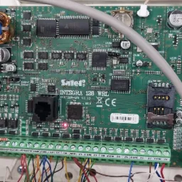 Centrala alarmowa Satel Integra 128 WRL z widoczną płytą główną, elementami elektronicznymi, gniazdem SIM i listwą zaciskową z podłączonymi przewodami.