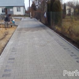 Perfektbud Bartlomiej Nowakowski - Układanie szarej kostki brukowej typu I na posesji, widoczny pracownik przy betoniarce i częściowo ułożona nawierzchnia z ciemniejszymi elementami dekoracyjnymi po bokach.