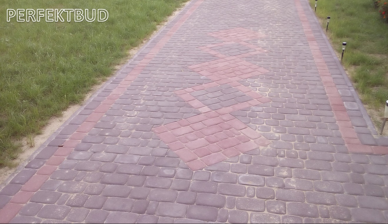 Ułożona ścieżka z kostki brukowej w odcieniach szarości i czerwieni, z dekoracyjnym wzorem rombów wzdłuż drogi, obok trawnik i małe lampki solarne.