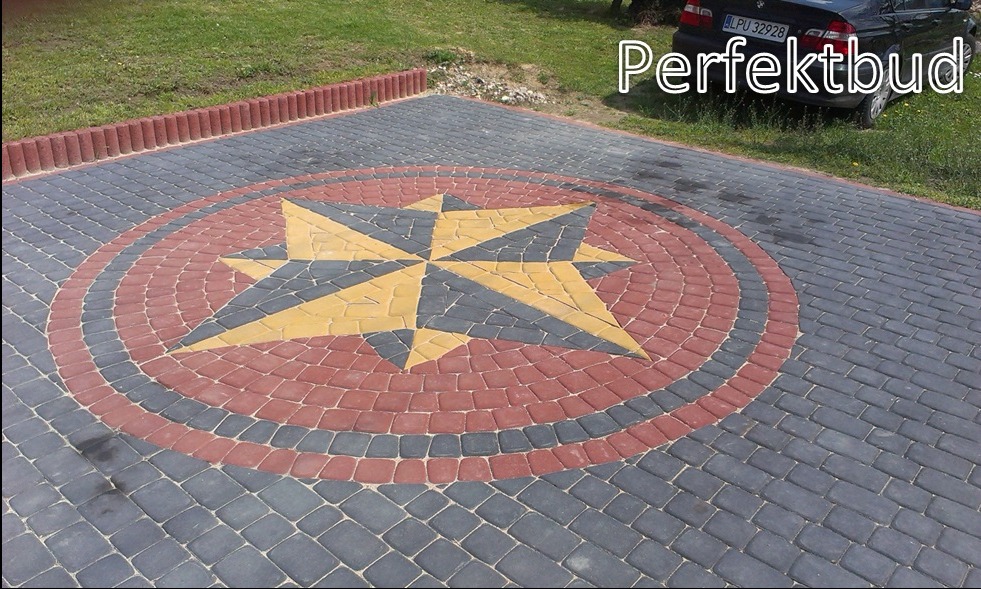 Ułożona kostka brukowa z wzorem rozety w kolorach żółtym, czerwonym i szarym, obrzeże z czerwonych palisad, trawnik i fragment samochodu w tle.