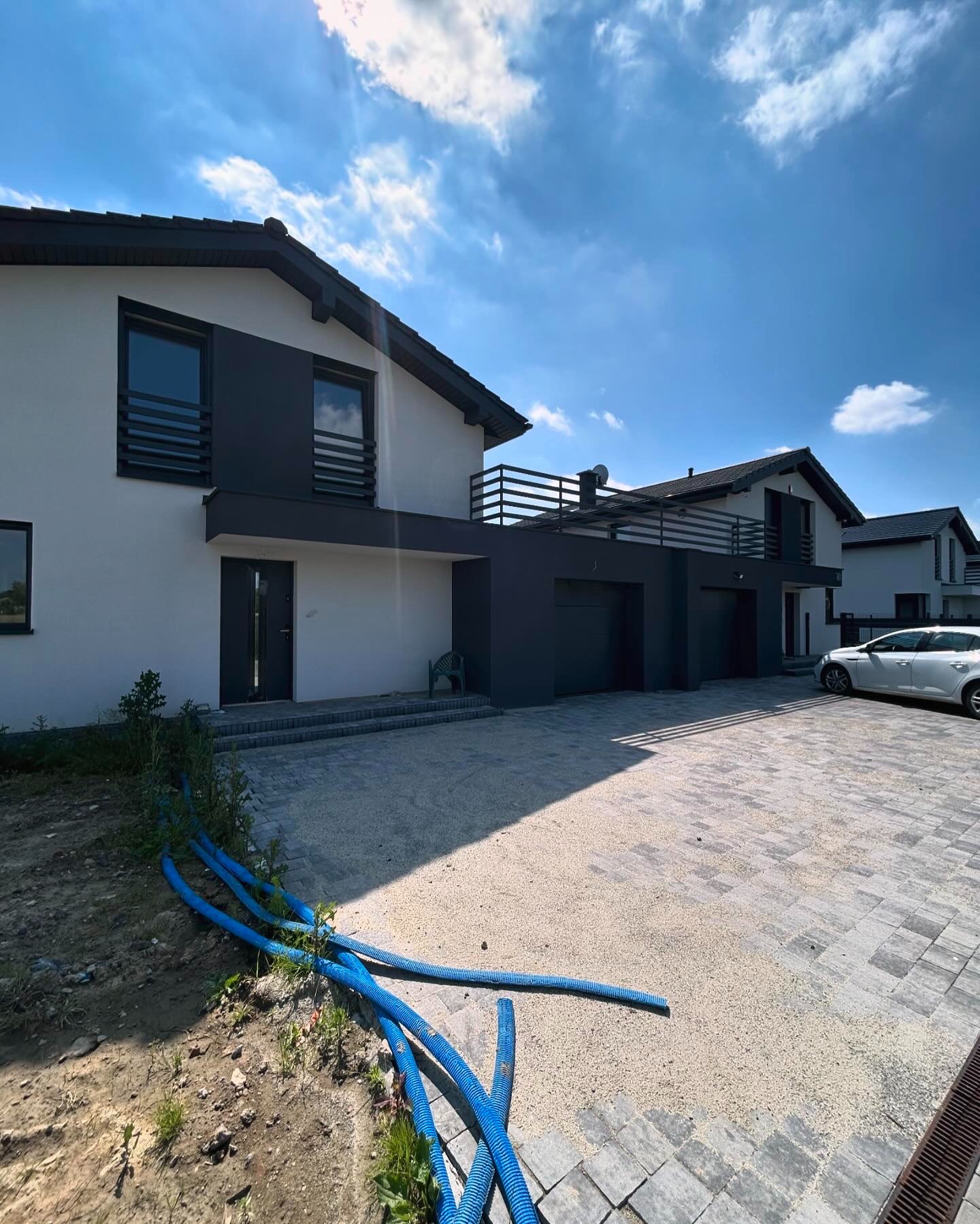 Nowoczesne domy jednorodzinne z balkonami zabezpieczonymi balustradami, szara elewacja, błękitne rury na pierwszym planie.