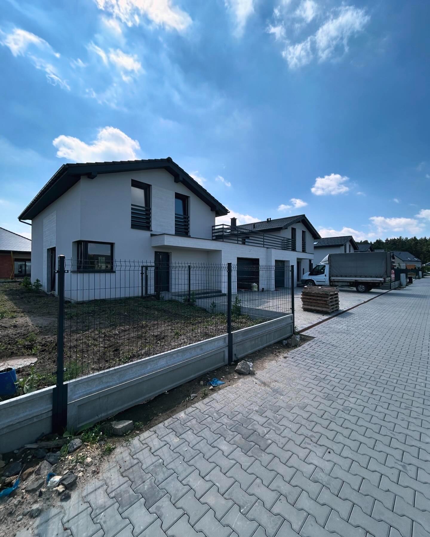Nowoczesne, dwukondygnacyjne domy jednorodzinne w Orzeszu, zabezpieczone panelowym ogrodzeniem z podmurówką betonową, widok z boku na posesję i chodnik z kostki brukowej.