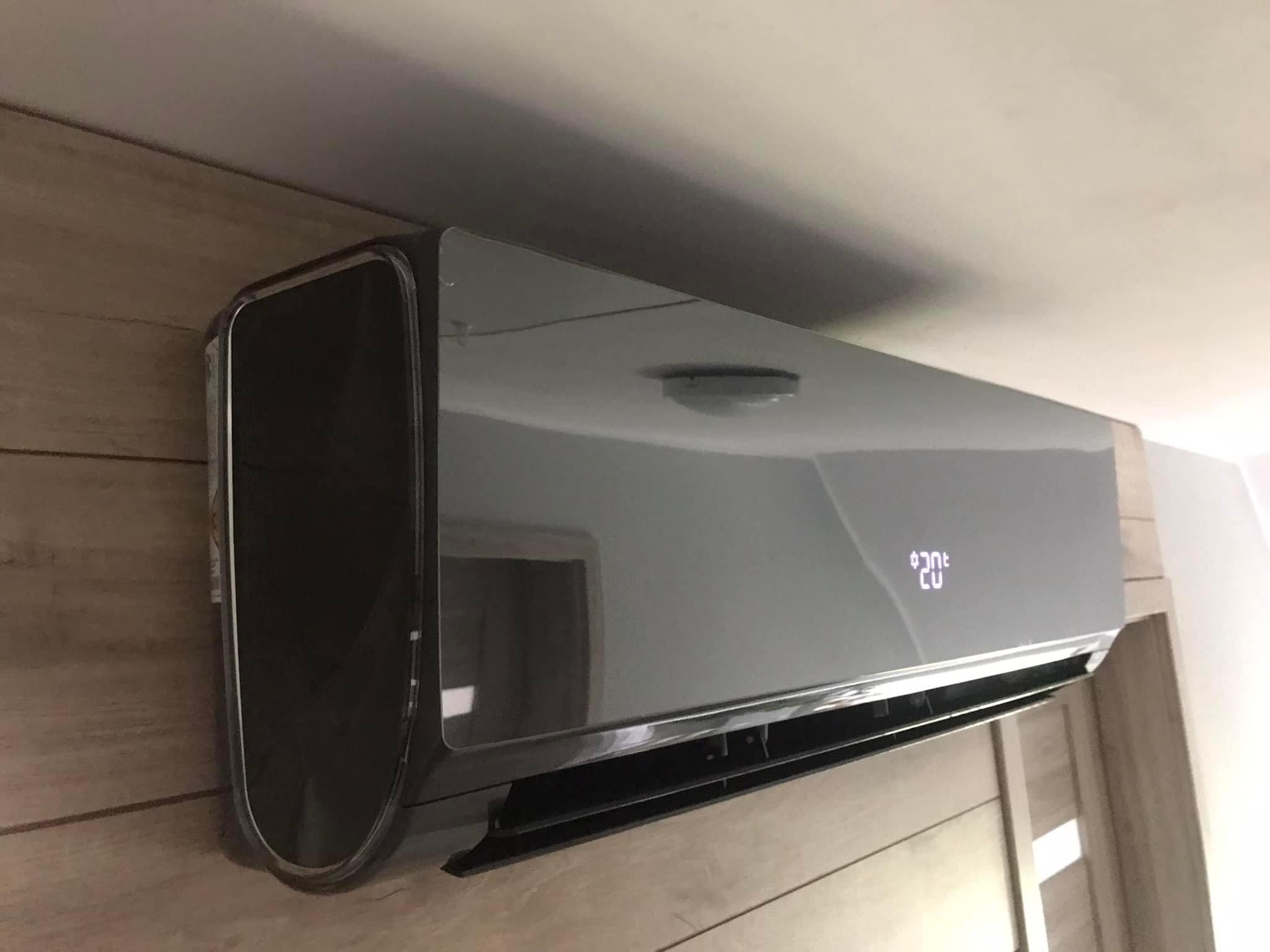 Czarny klimatyzator ścienny z wyświetlaczem ustawionej temperatury, zamontowany na ścianie z paneli drewnopodobnych.