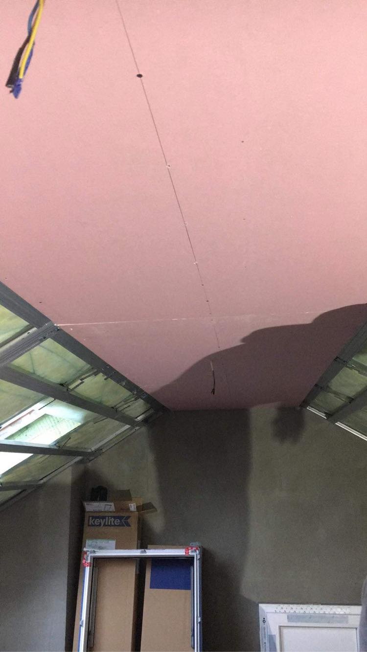 Montaż płyt kartonowo-gipsowych na metalowej konstrukcji stropu poddasza, widoczne przewody elektryczne i kartony z logo firmy Keylite.