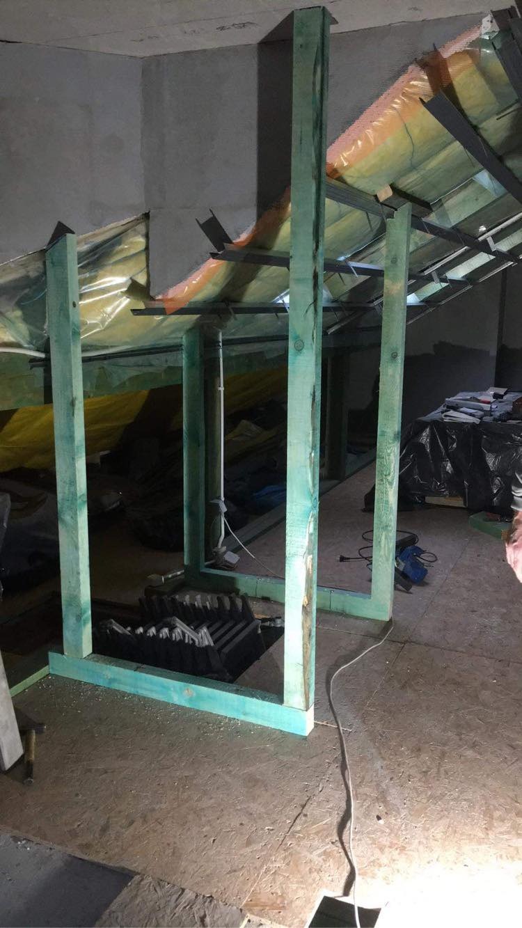 Wnętrze w trakcie ocieplania poddasza: widoczne drewniane ramy konstrukcyjne pomalowane na zielono, folia izolacyjna i metalowe profile pod płytami gipsowo-kartonowymi, oraz porozrzucane narzędzia...