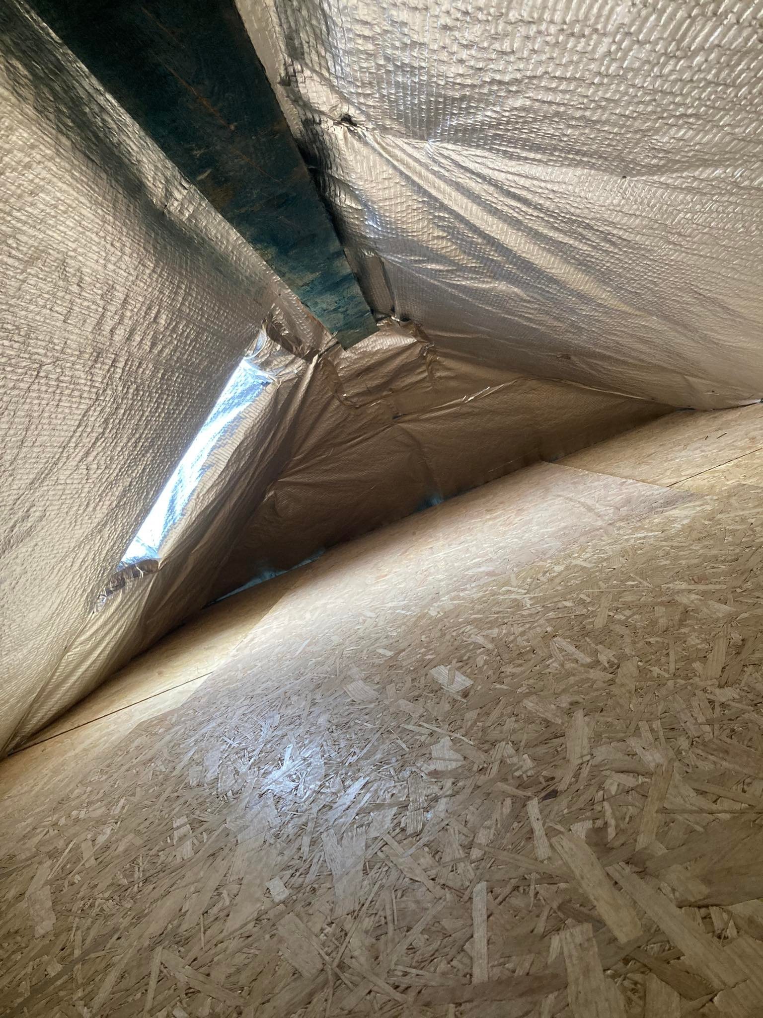 Wnętrze poddasza z widoczną izolacją termiczną (folia aluminiowa) i płytami OSB na ścianach szczytowych.