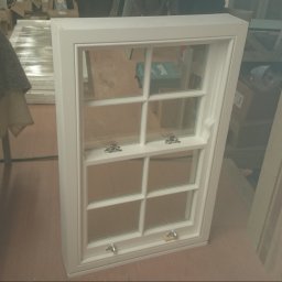 Tomasz Gorski - Białe, drewniane okno skrzynkowe z sześcioma szybami, widoczne okucia, w tle elementy warsztatu.