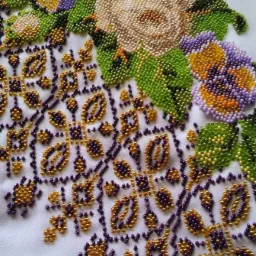 Ręcznie wykonany haft koralikowy z motywem kwiatowym na białym tle, prezentujący róże i bratki w odcieniach fioletu, złota i zieleni.