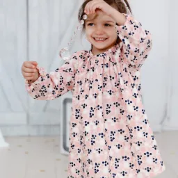 Uśmiechnięta dziewczynka w różowej sukience w kwiaty, bawiąca się szklanymi paciorkami, dopasowana opaska na włosach.